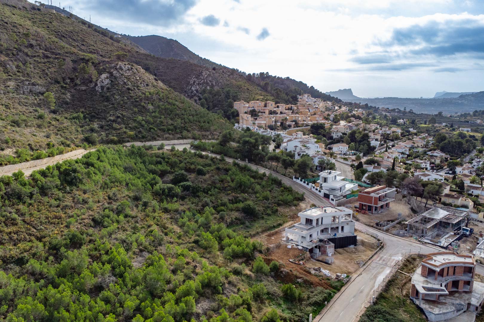 Vue aérienne du terrain à Monte Olímpico, illustrant l'infrastructure achevée, les villas environnantes en construction et le versant verdoyant face à la vallée.