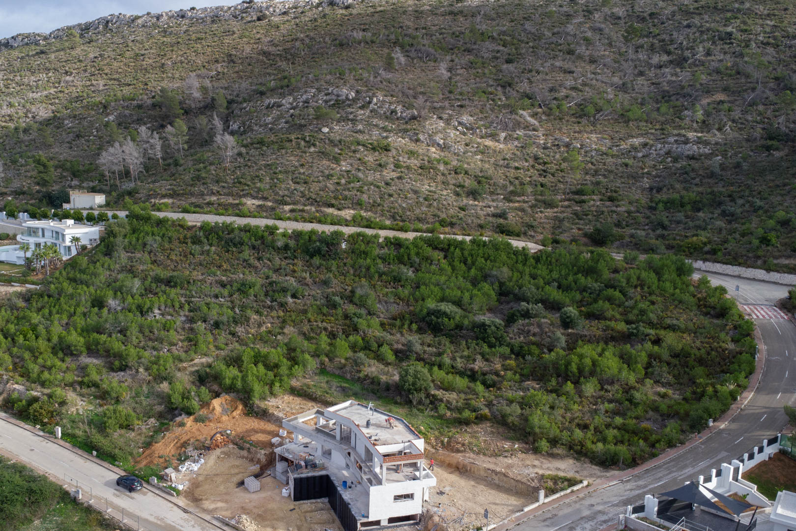 Vue aérienne du terrain à Monte Olímpico, illustrant l'infrastructure urbaine achevée et une villa en construction entourée de nature méditerranéenne.