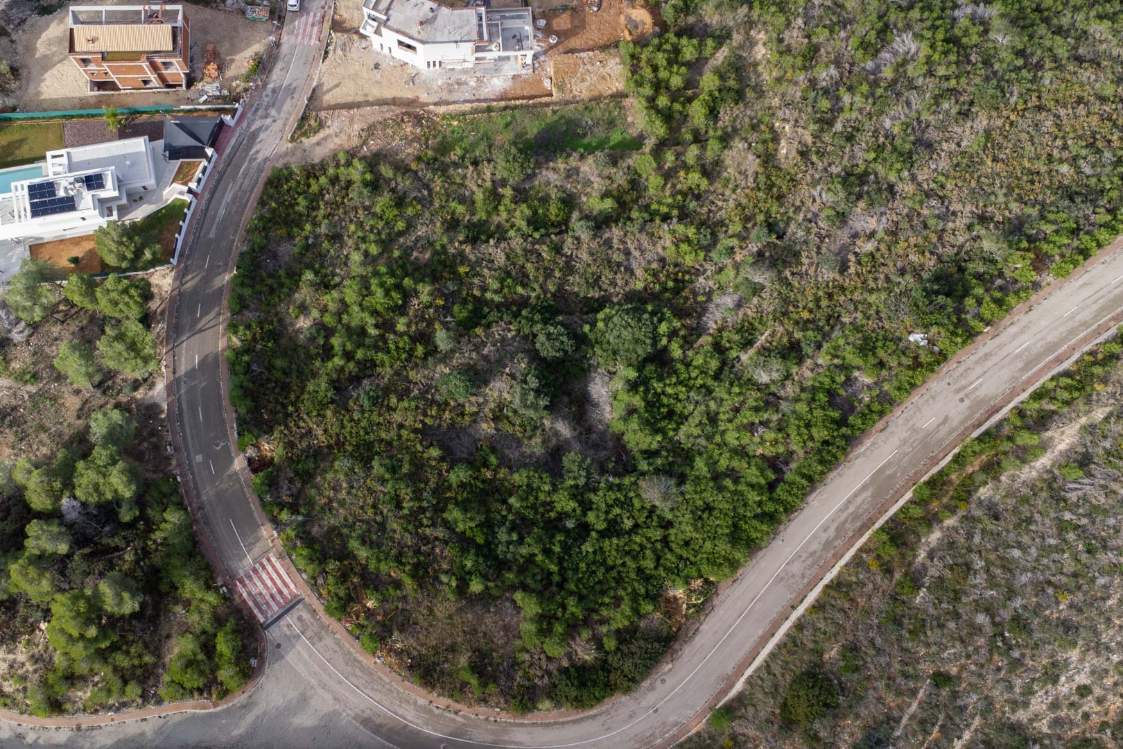 Vue aérienne zénithale du terrain urbain en angle, bordé par des rues pavées avec trottoirs et une végétation méditerranéenne dense à Monte Olímpico.
