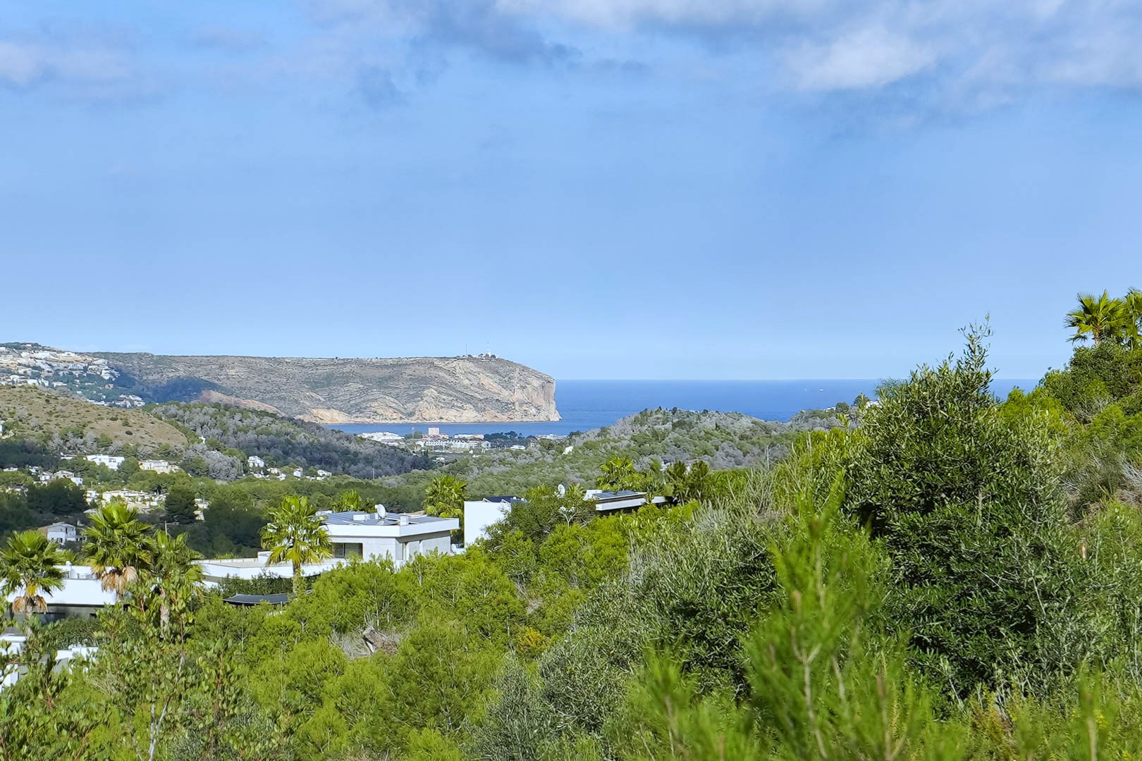 Vue panoramique depuis le terrain sur la mer Méditerranée et le Cabo de San Antonio, entourée de pins et de villas à l'architecture moderne.