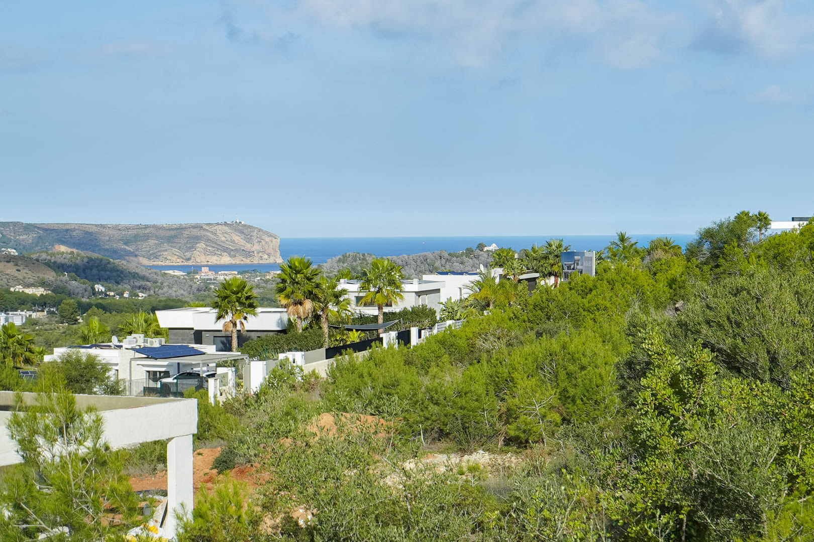 Vues panoramiques sur la mer Méditerranée et le Cabo de San Antonio depuis le terrain, entouré de villas modernes et d'une végétation locale dense.