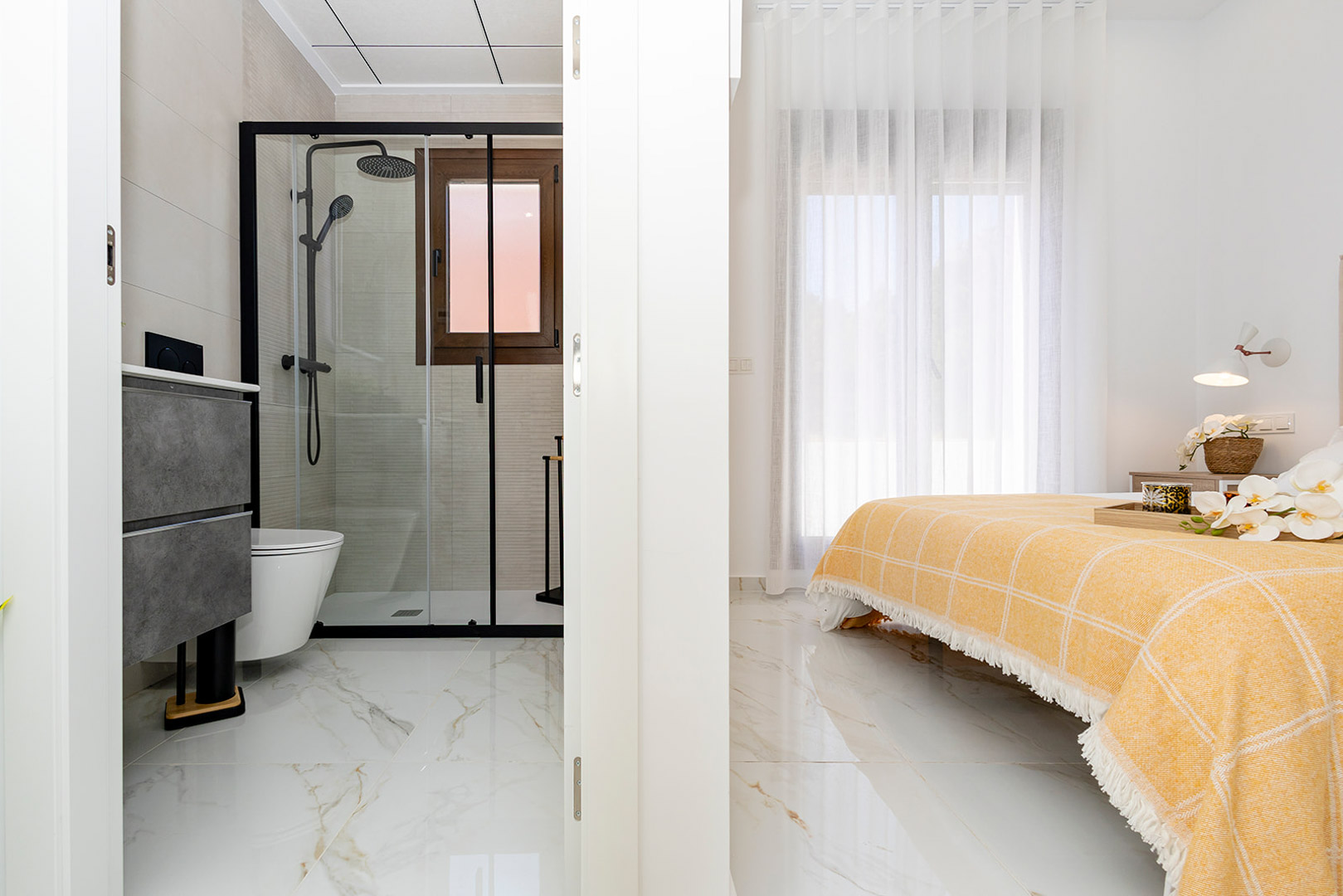 Chambre avec salle de bain attenante, sols en grès cérame effet marbre et douche à l'italienne avec robinetterie noire moderne.
