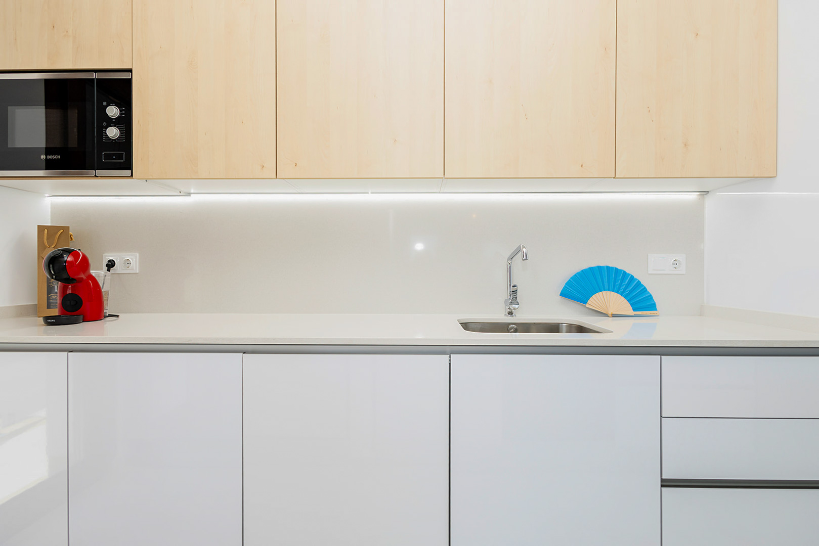 Cuisine moderne avec placards supérieurs en bois clair, meubles bas blancs, plan de travail en quartz et éclairage LED intégré.