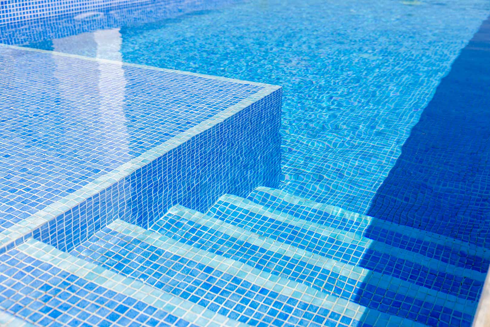 Gros plan de la piscine privée avec revêtement en mosaïque bleue, mettant en valeur les marches immergées et la limpidité de l'eau.