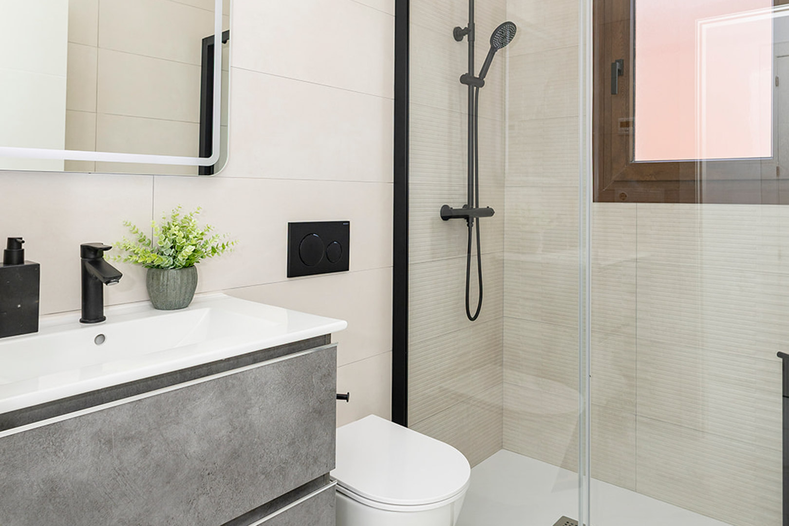 Salle de bain moderne avec meuble gris, robinetterie noire mate, WC suspendu et douche vitrée avec carrelage à relief linéaire.