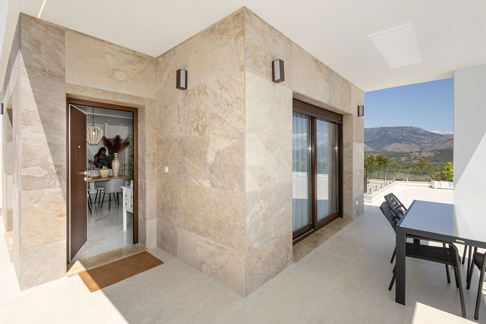 Terrasse extérieure avec revêtement en pierre naturelle, coin repas et vue sur les montagnes. L'entrée offre un accès direct à l'espace de vie intérieur.