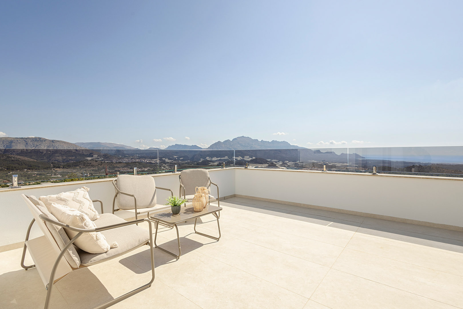 Terrasse solarium avec carrelage clair, garde-corps en verre et mobilier d'extérieur offrant une vue panoramique sur la mer et les montagnes.