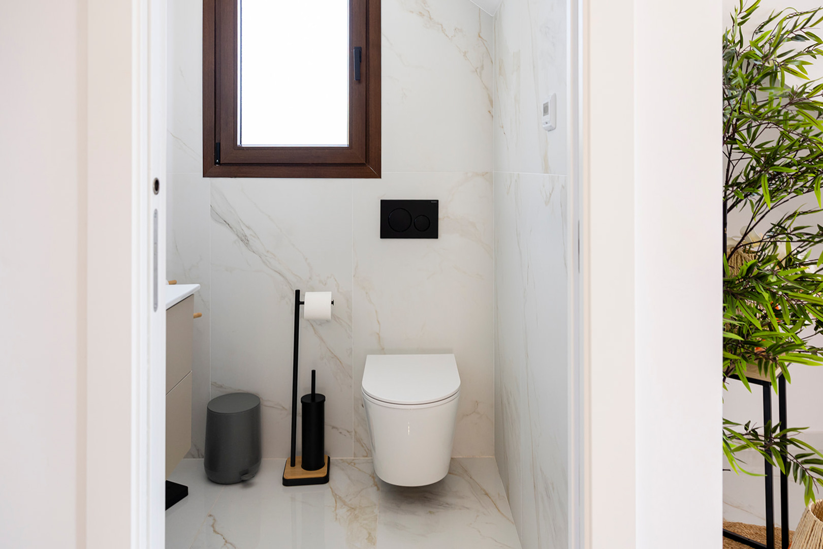 Toilettes invités avec carrelage effet marbre, WC suspendu et finitions noir mat. Une fenêtre à cadre en bois assure la ventilation naturelle.