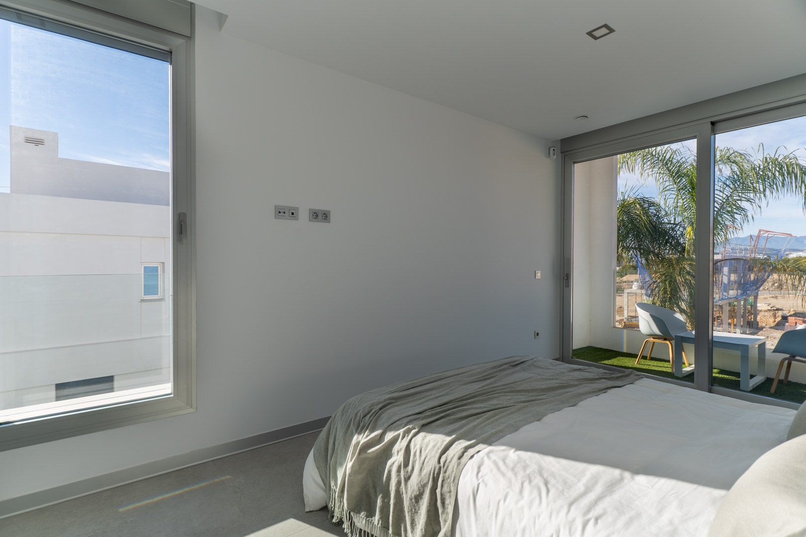 Chambre lumineuse avec accès direct à une terrasse privée en gazon synthétique. Design minimaliste avec sol en grès cérame gris et menuiserie en aluminium.