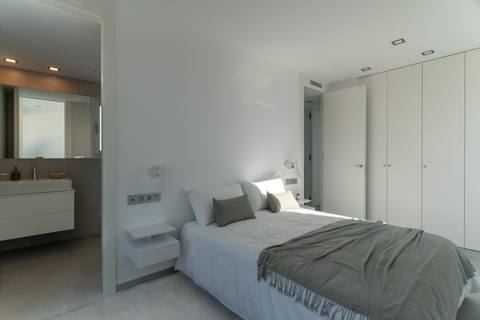 Chambre principale avec salle de bain attenante, placards intégrés et design minimaliste épuré avec éclairage encastré au plafond.
