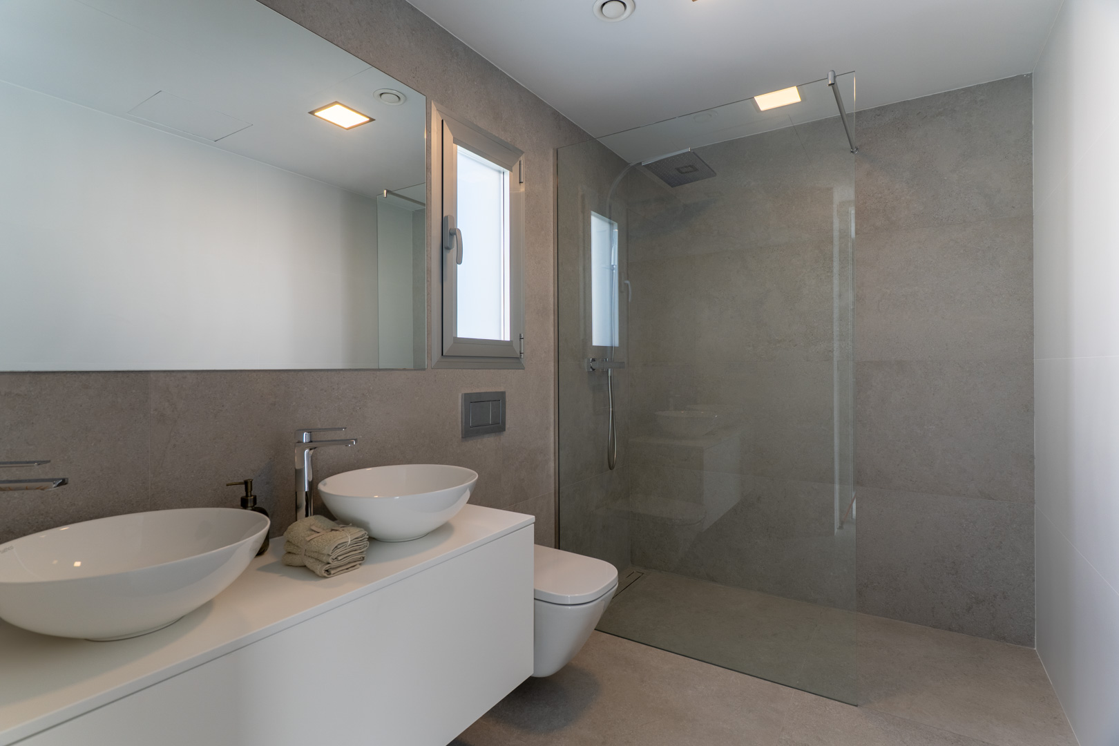 Salle de bain moderne avec carrelage gris effet pierre, double vasque sur meuble suspendu blanc et douche à l'italienne avec paroi en verre fixe.