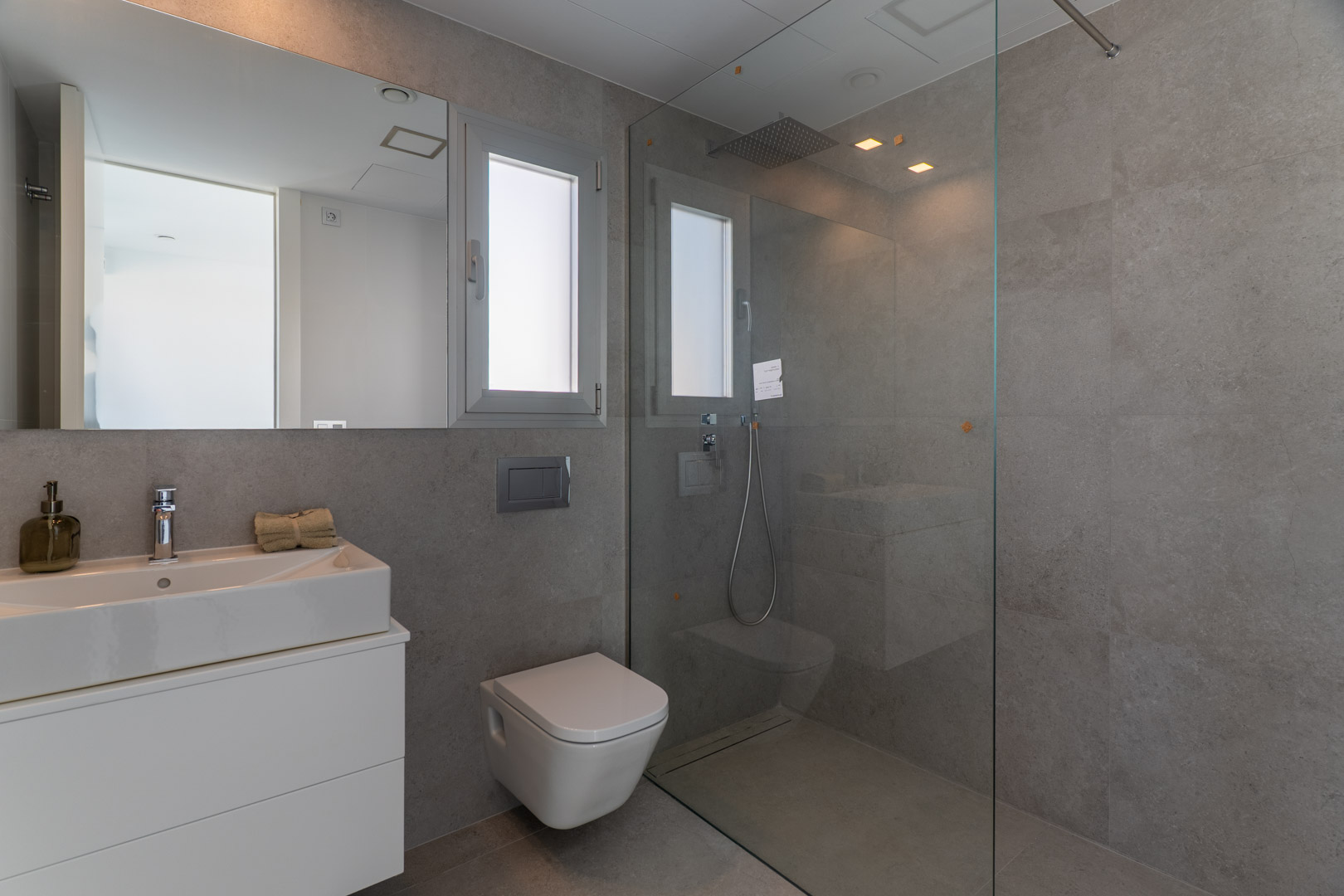 Salle d'eau contemporaine avec carrelage gris, douche à l'italienne, paroi en verre, WC suspendu et lavabo intégré sur meuble blanc minimaliste.