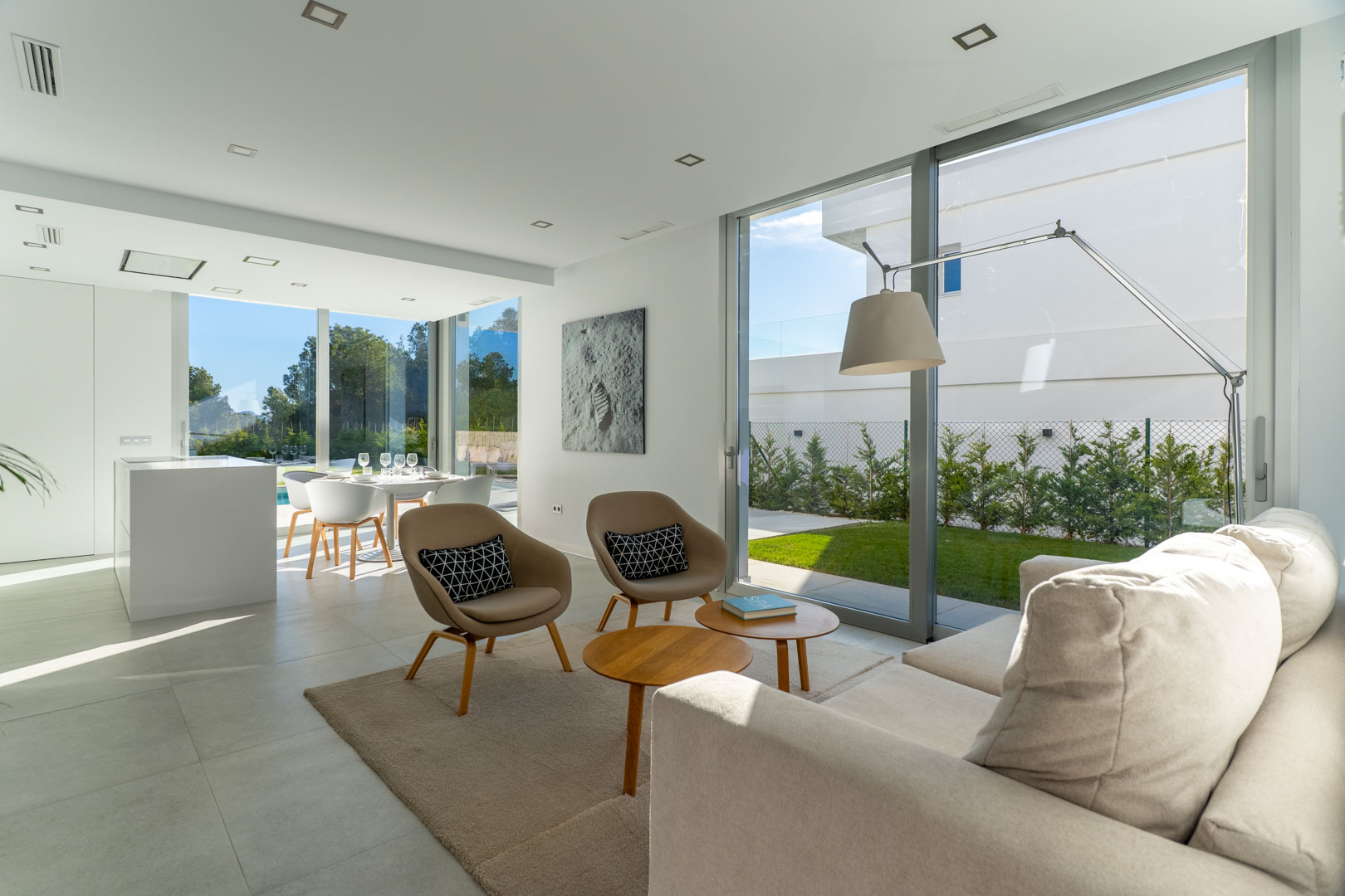 Salon ouvert et lumineux avec de grandes baies vitrées, un mobilier contemporain aux tons naturels et une vue dégagée sur le jardin extérieur.