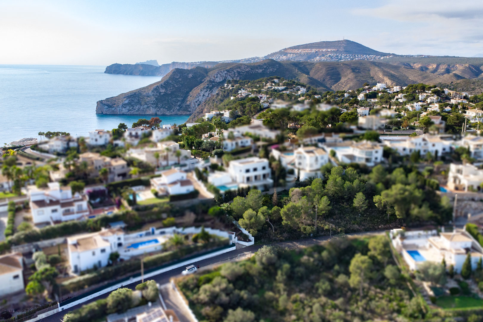 Vue aérienne avec effet miniature du quartier Granadella-Ambolo, montrant les villas blanches et la côte sauvage de Jávea bordée par la mer.
