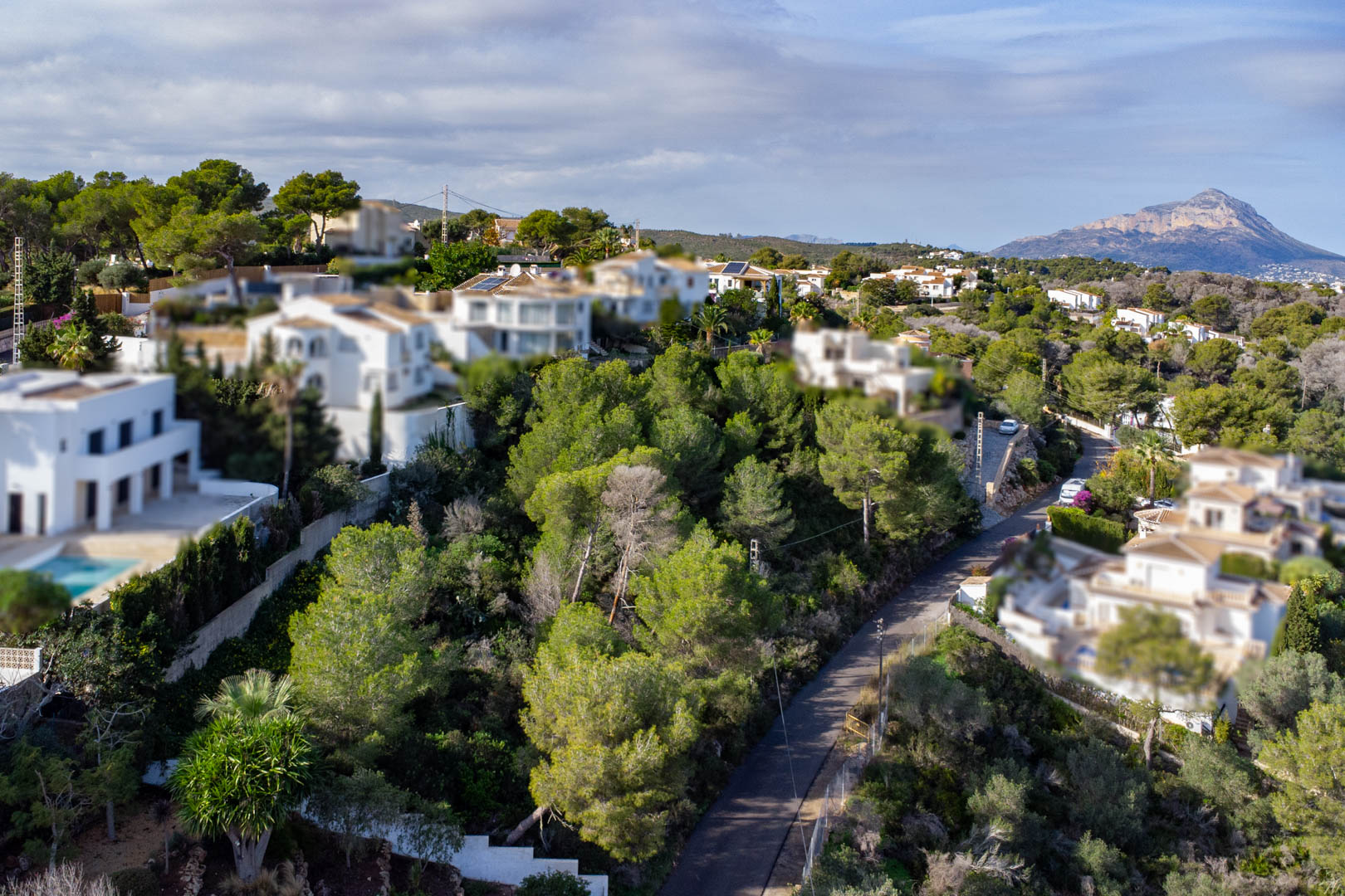Vue aérienne du terrain boisé en pente, entouré de villas blanches et offrant une vue dégagée sur le massif du Montgó à l'horizon.