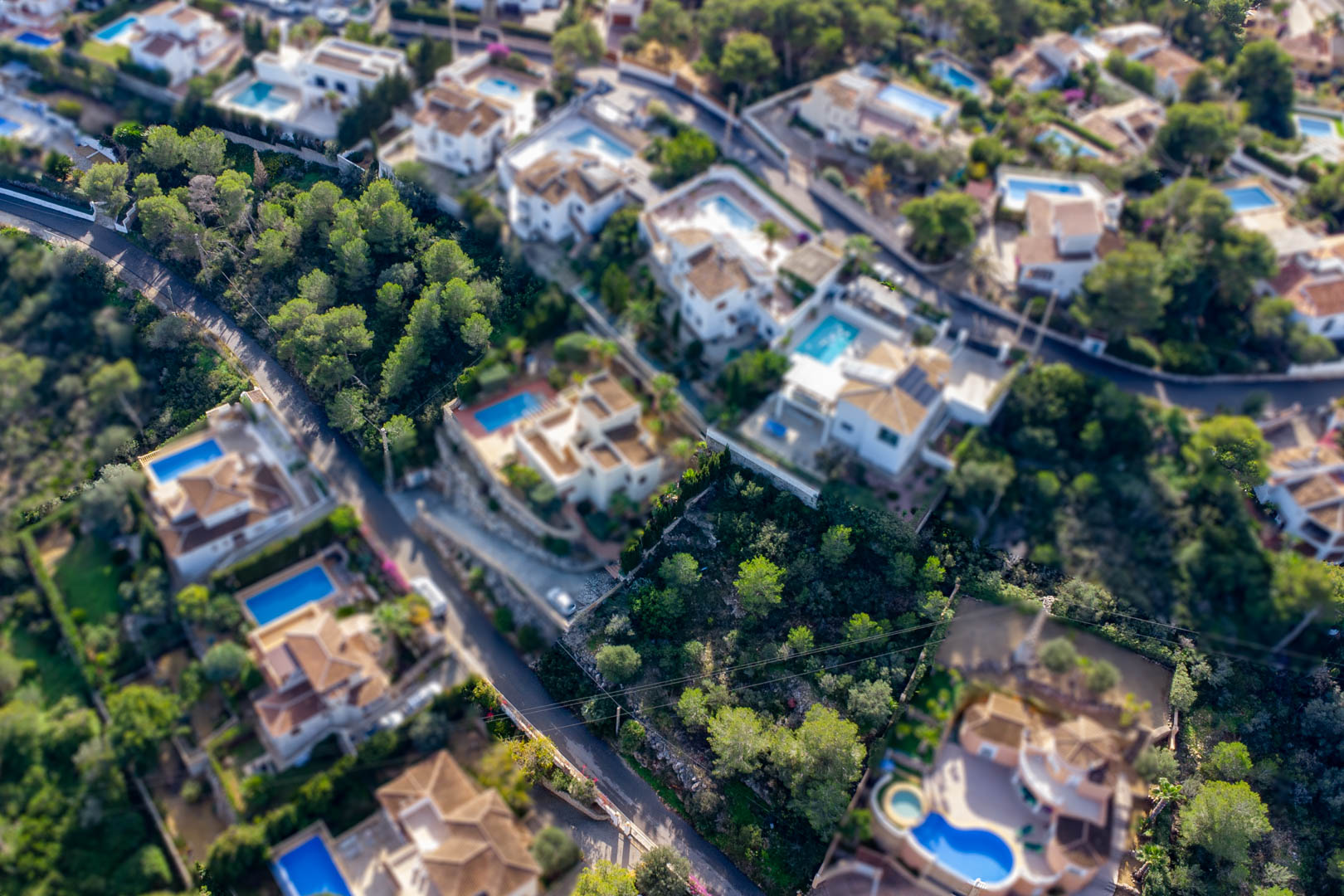 Vue aérienne du terrain à bâtir à Granadella-Ambolo, situé au cœur d'un quartier résidentiel avec villas, piscines privées et une pinède dense.