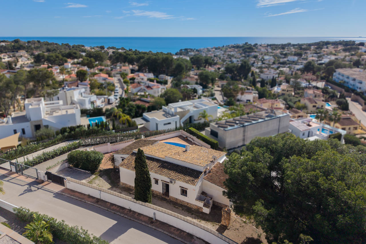 Vue aérienne de la villa à Benissa Costa, soulignant son architecture méditerranéenne, son terrain privé avec cyprès et une vue dégagée sur la mer.