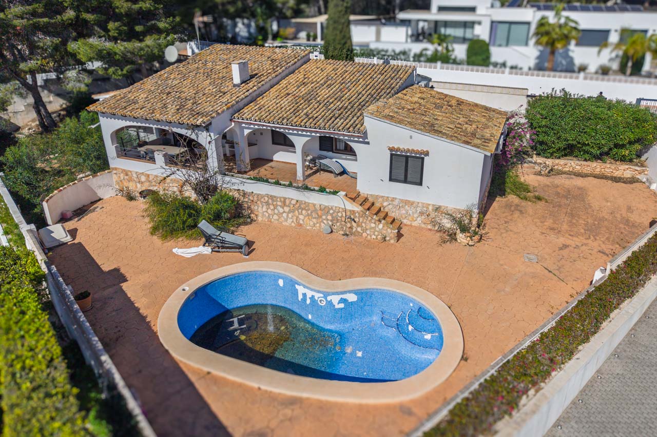 Vue aérienne de la villa avec piscine de forme organique, vastes terrasses pavées et porches à arches. L'extérieur présente des murs en pierre naturelle et un toit en tuiles traditionnelles.