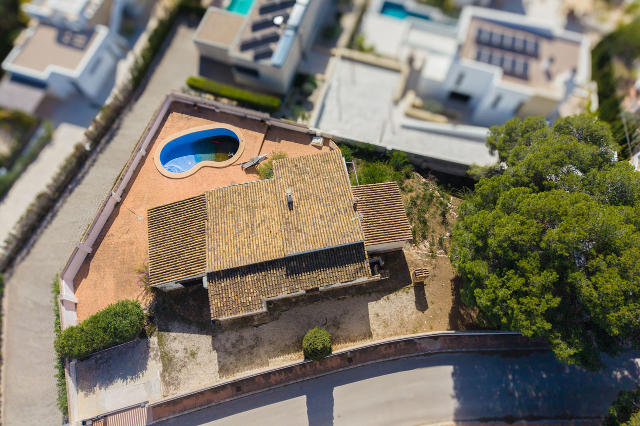 Vue aérienne de la villa montrant son toit en tuiles, sa piscine de forme organique et son terrain plat situé dans un quartier résidentiel calme.
