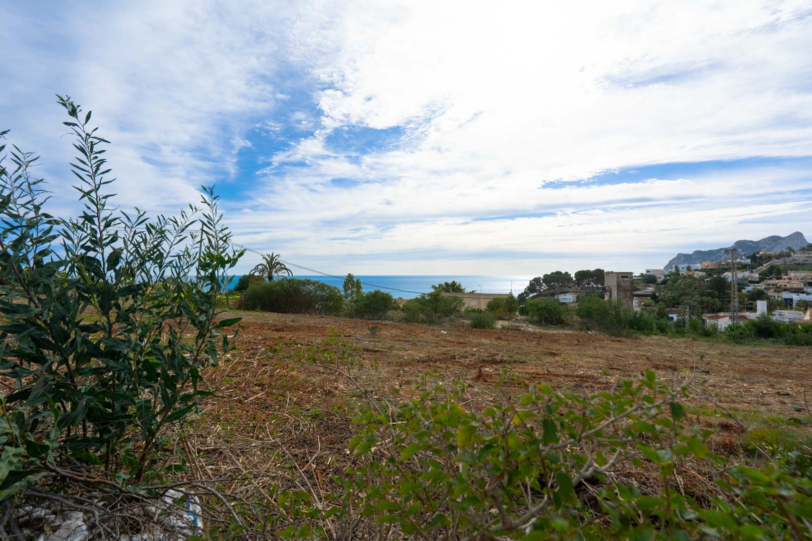 Terrain en pente offrant une vue panoramique sur la mer Méditerranée et les montagnes environnantes, situé à proximité d'une zone résidentielle calme.