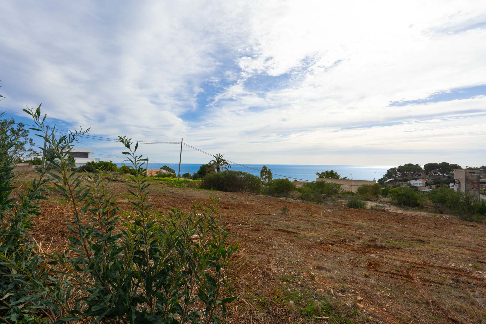 Terrain surélevé offrant une vue panoramique sur la mer, avec un sol dégagé et une végétation méditerranéenne sous un ciel lumineux.