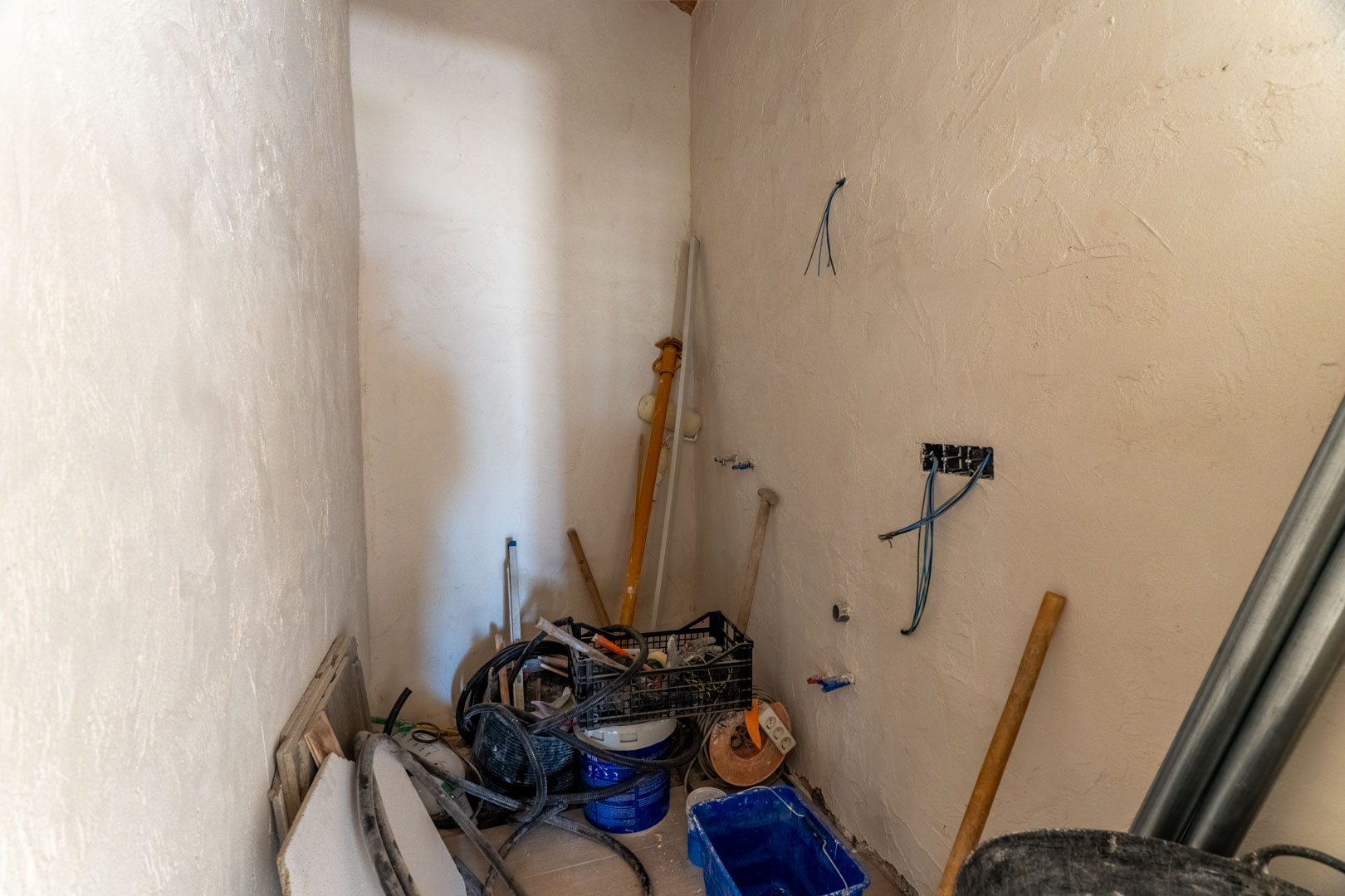 Pièce intérieure en cours de rénovation avec murs enduits, câblage électrique apparent et divers matériaux de construction pour les finitions.