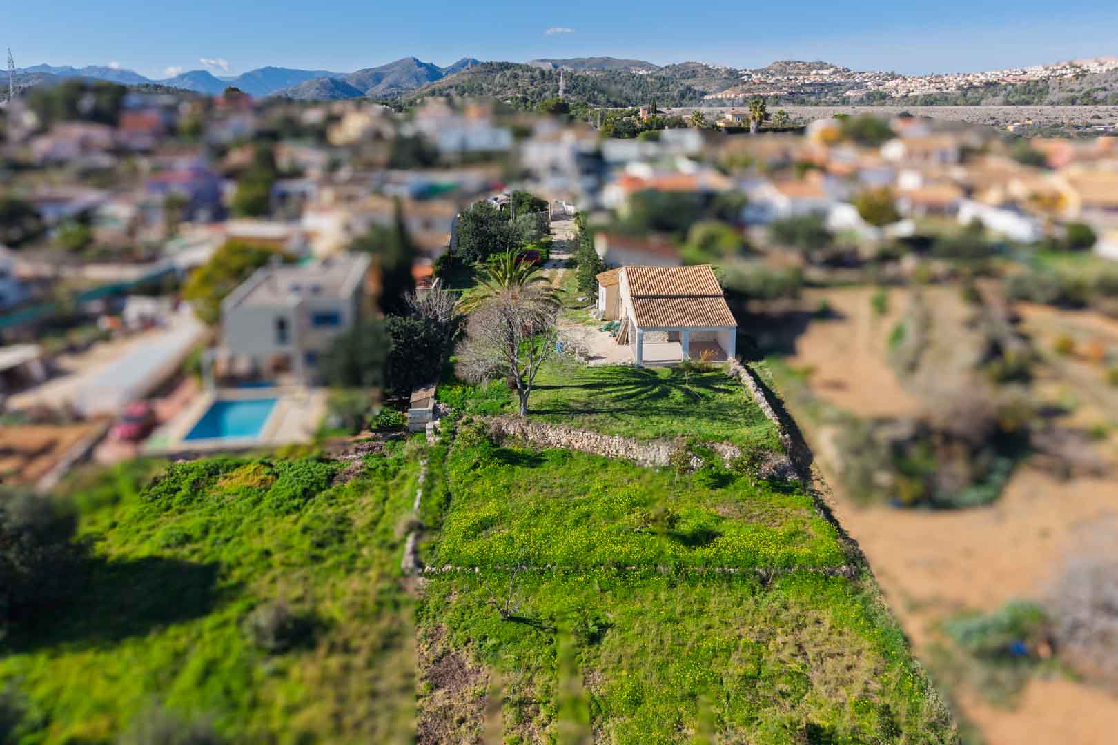 Vue aérienne de la finca montrant le toit en tuiles rénové et la naya, sur une parcelle allongée avec des murs en pierre sèche et vue sur les montagnes environnantes.