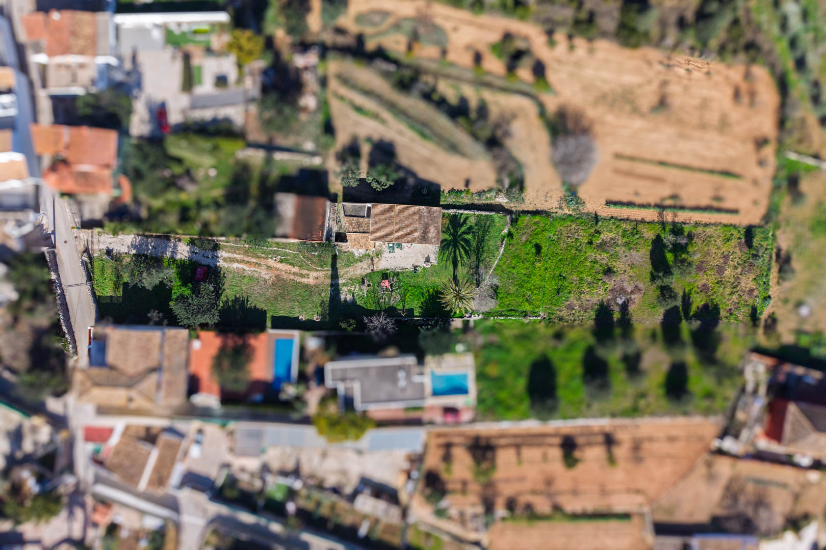 Vue aérienne zénithale de la propriété et de sa parcelle rectangulaire, montrant la maison centrale au toit de tuiles et les jardins avec palmiers.