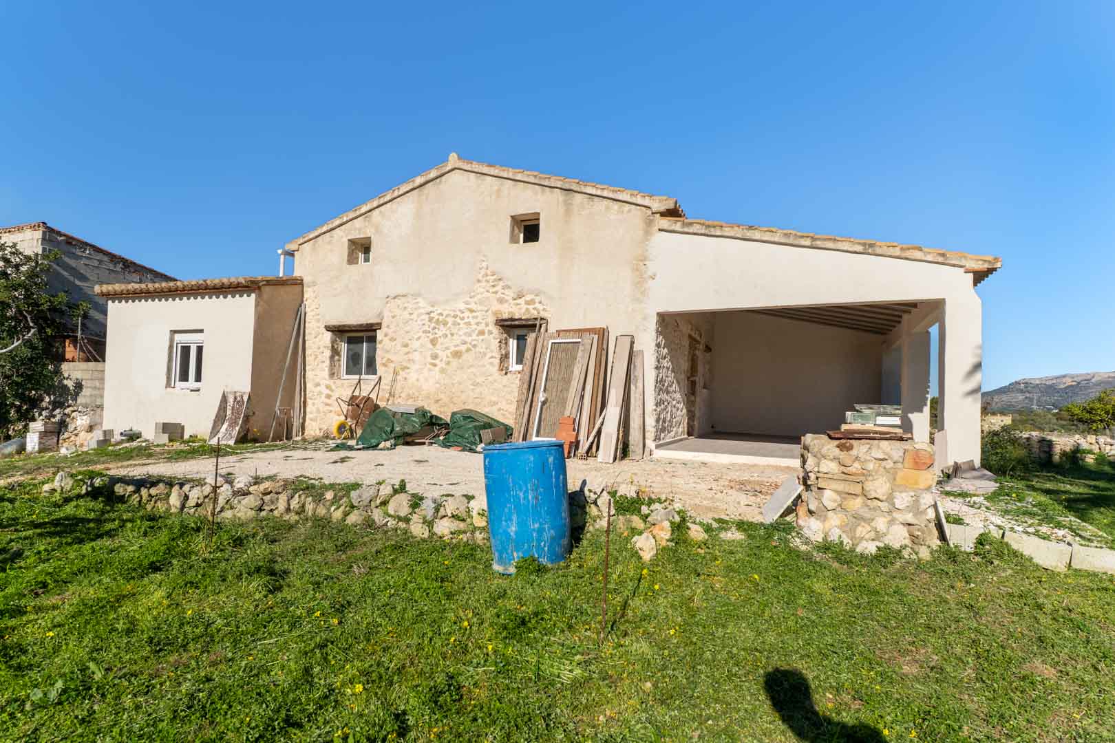 Vue extérieure de la façade avec murs en pierre d'origine, naya couverte et terrain en terrasses, illustrant le projet de rénovation de la finca.