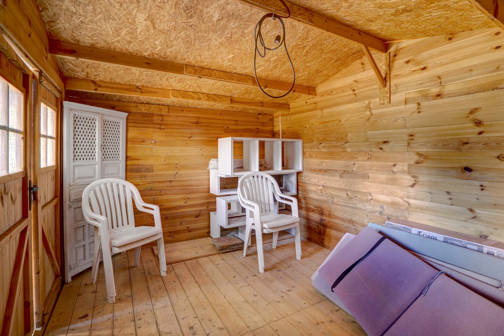 Abri de jardin en bois avec parois lambrissées, plafond en OSB et sol en planches, offrant un espace de rangement supplémentaire fonctionnel.