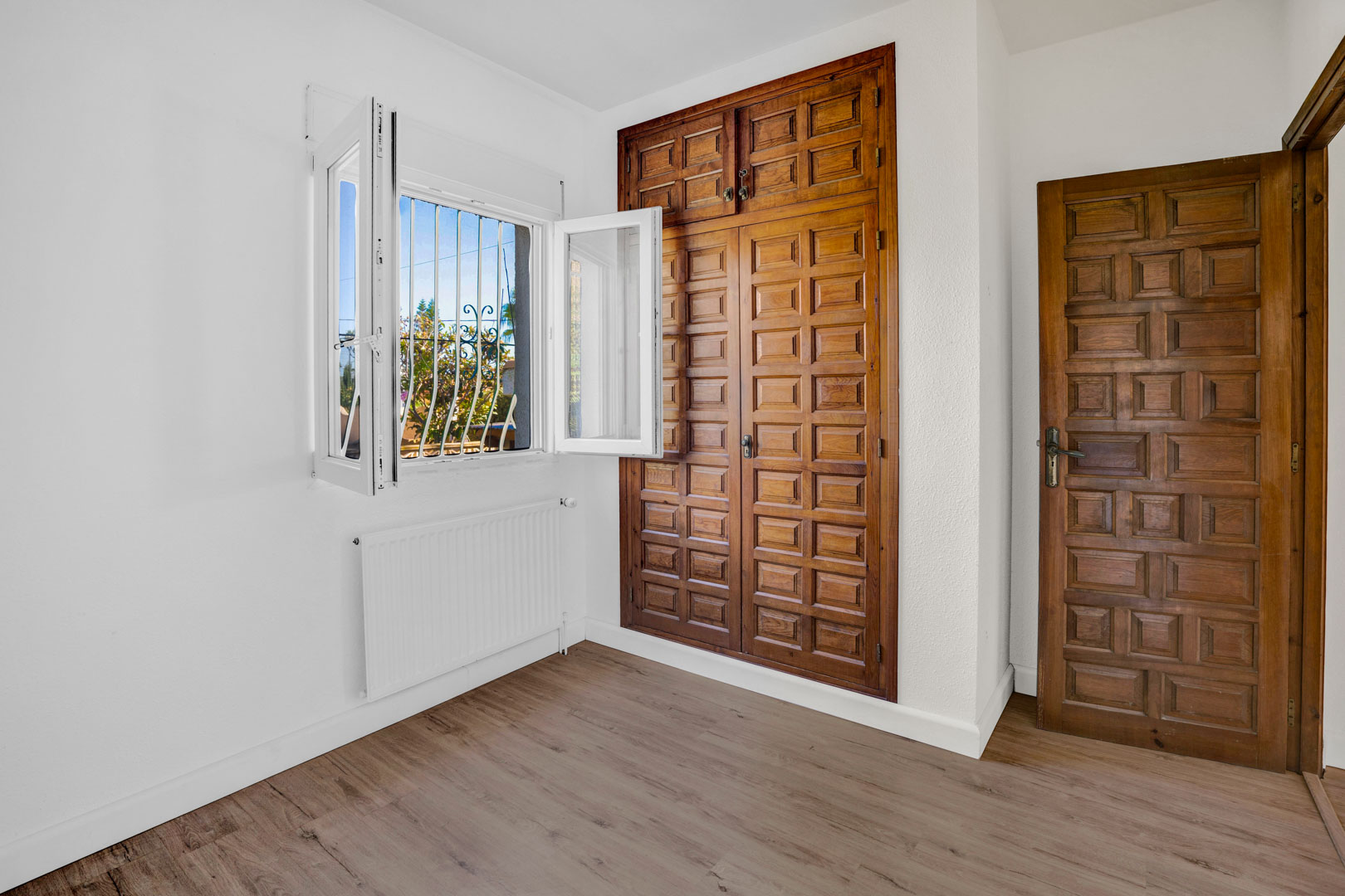 Chambre avec placard intégré en bois sculpté, sol stratifié, radiateur de chauffage central et fenêtre offrant une luminosité naturelle.
