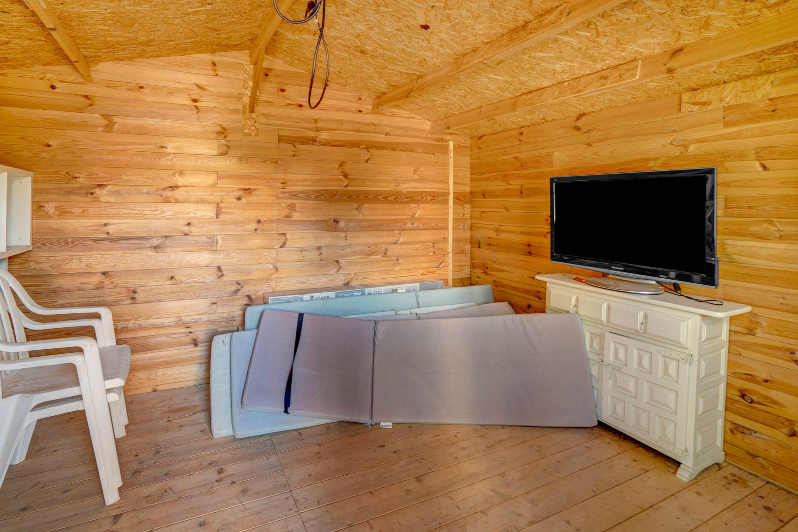 Dépendance de jardin en bois avec parois en pin, comprenant un buffet blanc avec télévision et un espace de rangement pour le mobilier d'extérieur.