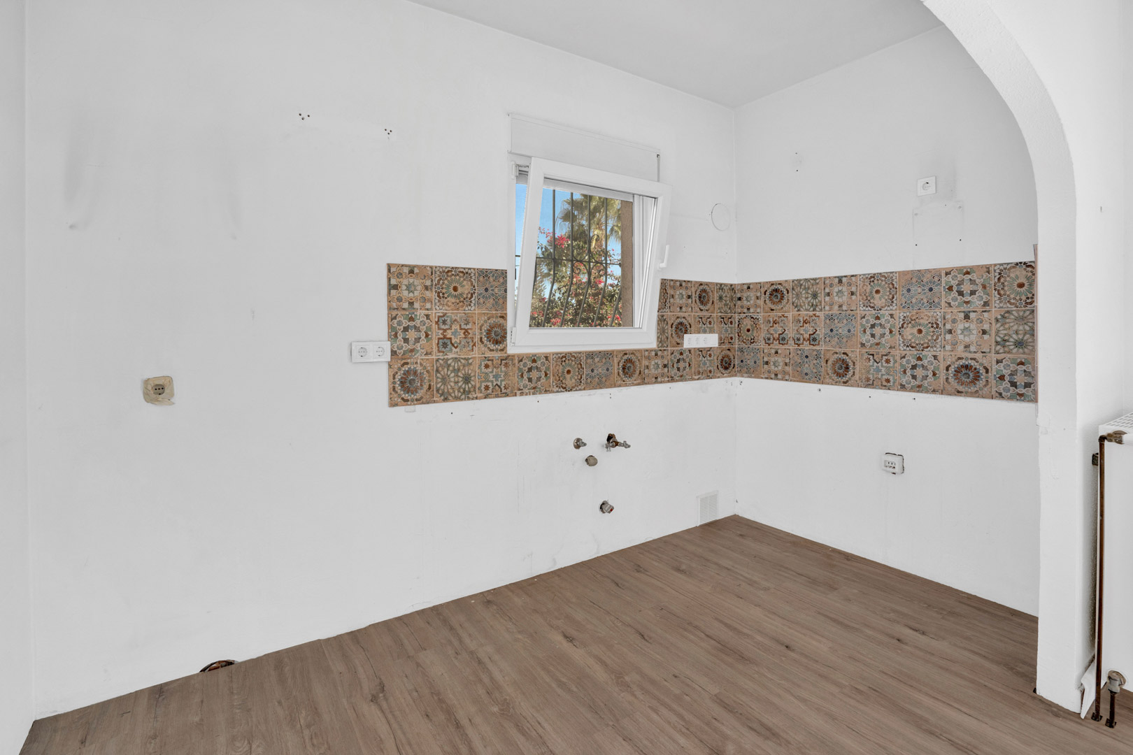 Espace cuisine avec sol stratifié, carreaux décoratifs et fenêtre offrant une lumière naturelle.