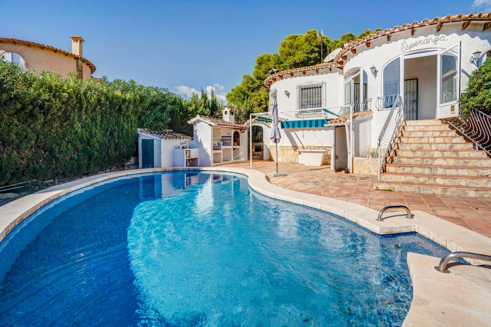 Espace piscine privée avec terrasse en terre cuite, cuisine d'été avec barbecue et escalier en pierre menant à la véranda principale.