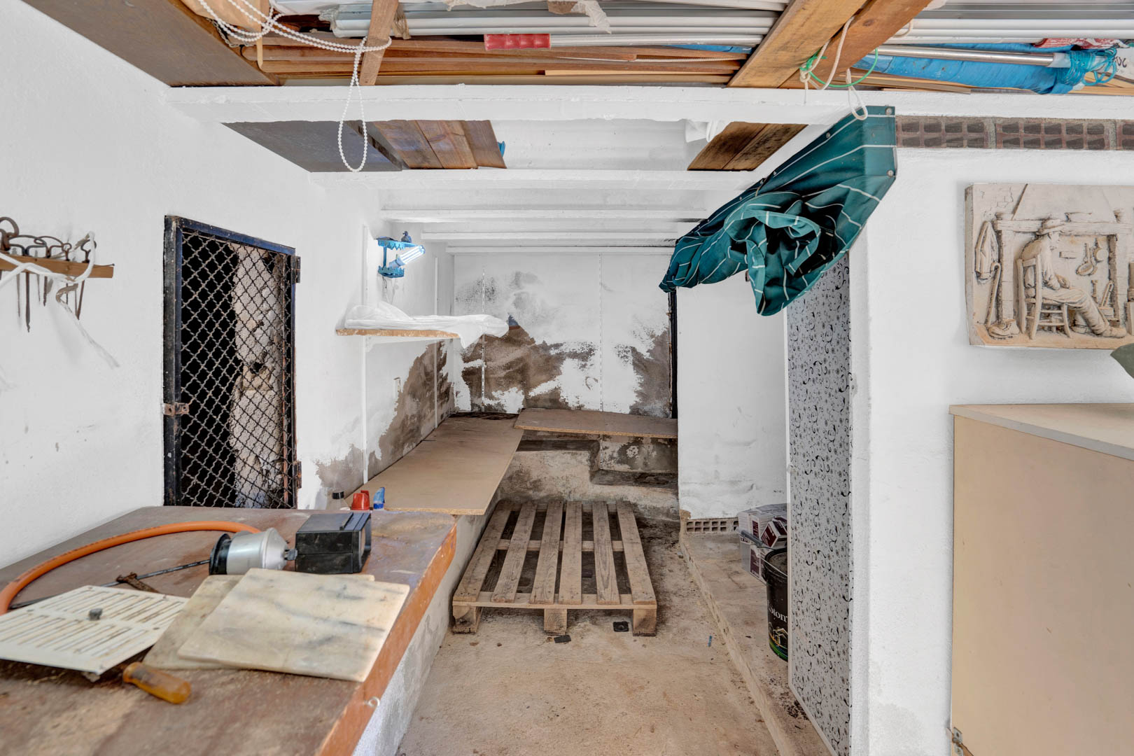 Semi-sous-sol fonctionnel utilisé comme espace de rangement et atelier, avec poutres apparentes, établis en bois et une zone de stockage polyvalente.