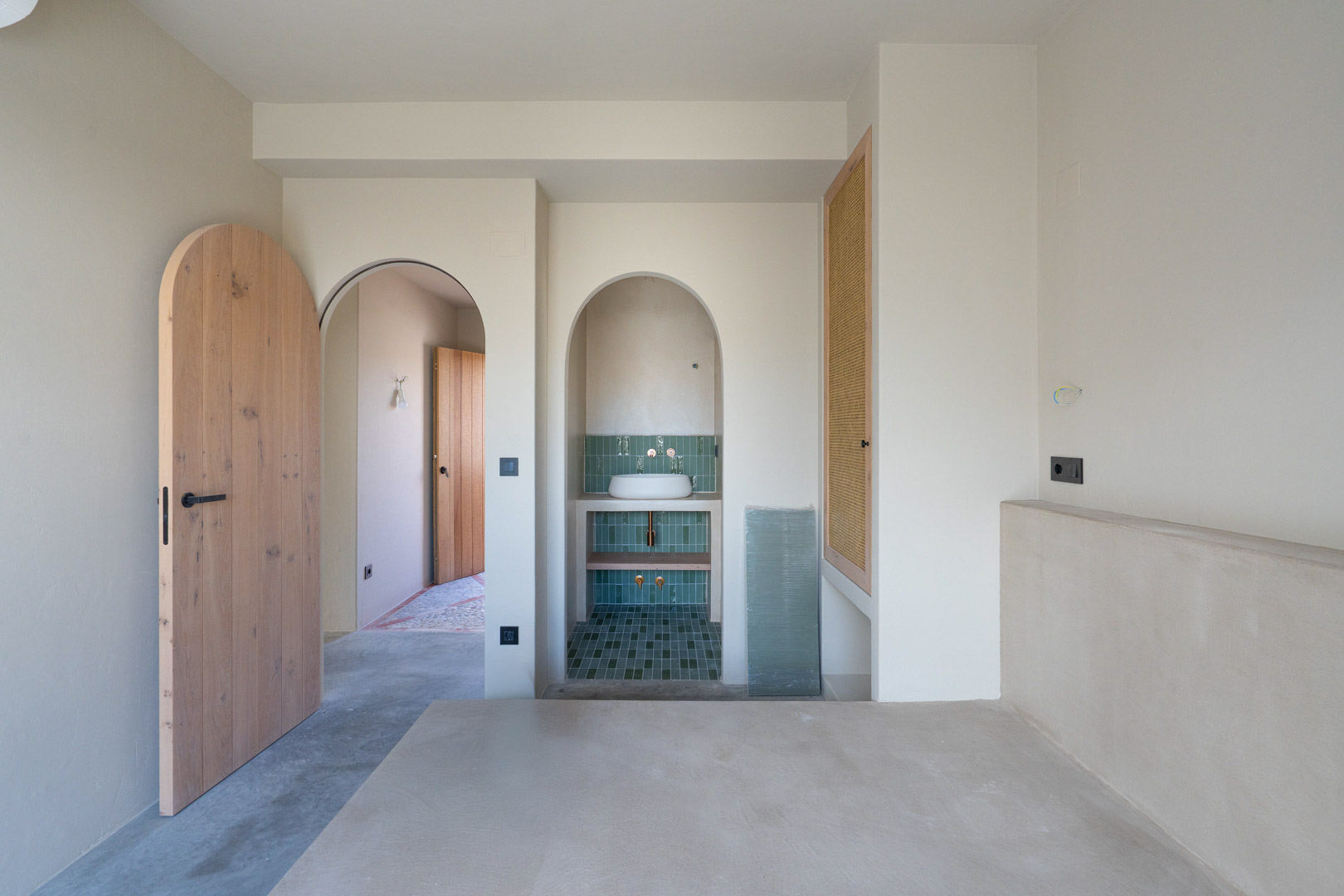 Chambre avec finitions en argile Matteo Brioni, portes cintrées en chêne massif et coin lavabo intégré avec carrelage vert et sol en béton poli.