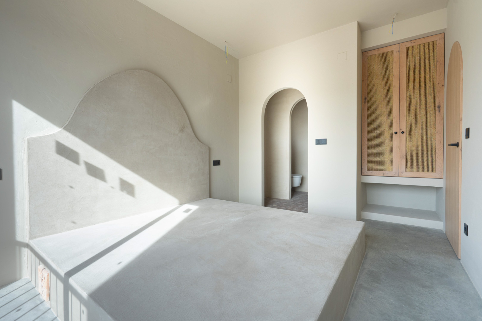 Chambre avec sommier intégré et tête de lit en argile. Comprend des armoires en chêne avec cannage et des passages voûtés menant à la salle de bain attenante.