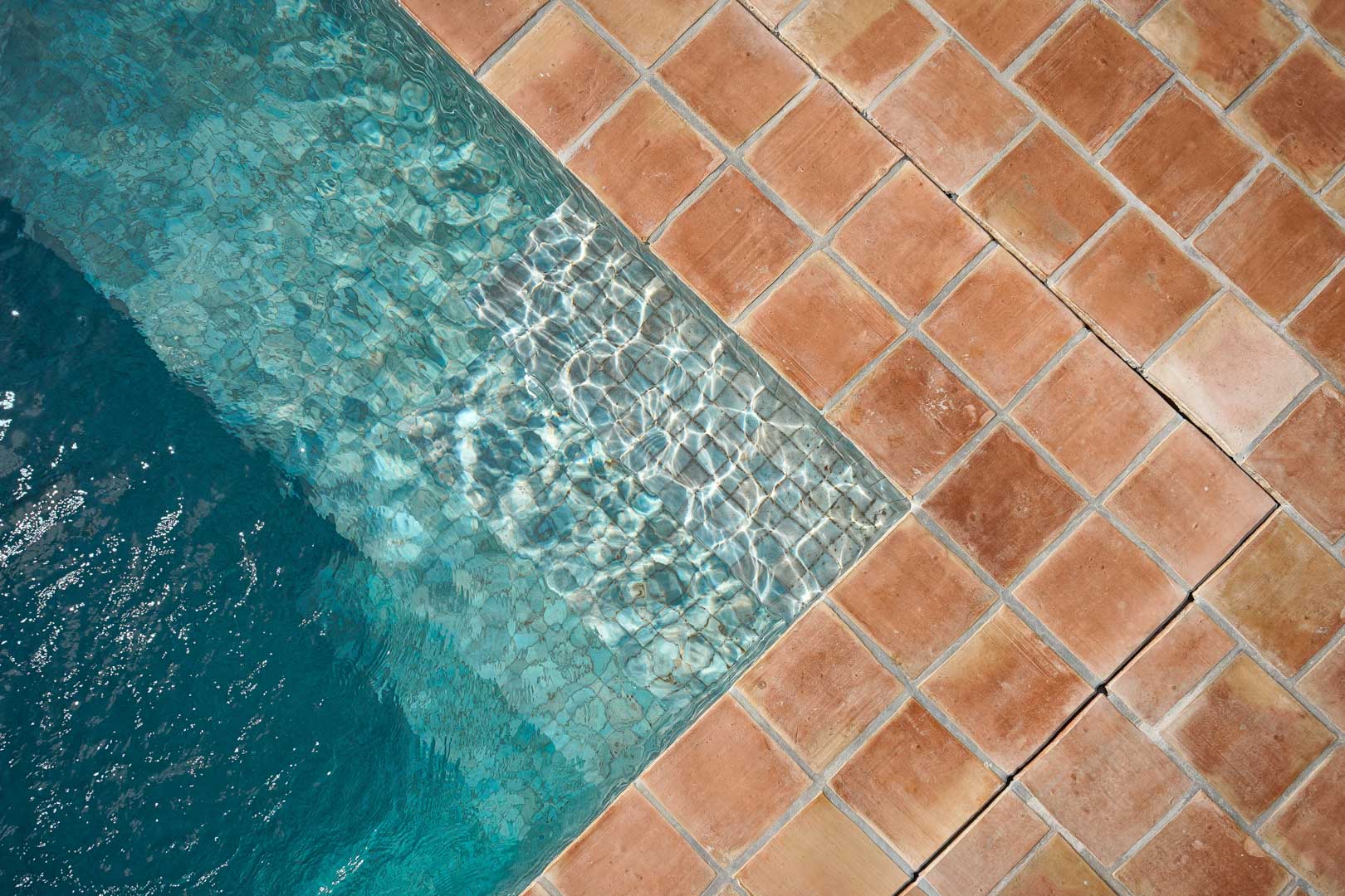 Détail de l'angle de la piscine avec des carreaux en terre cuite naturelle, soulignant le contraste entre les tons terreux et l'eau cristalline.