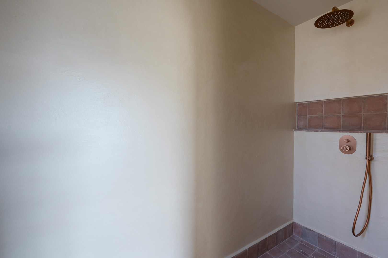 Douche moderne avec murs en argile Matteo Brioni, robinetterie cuivrée et finitions en terre cuite pour une esthétique méditerranéenne naturelle.
