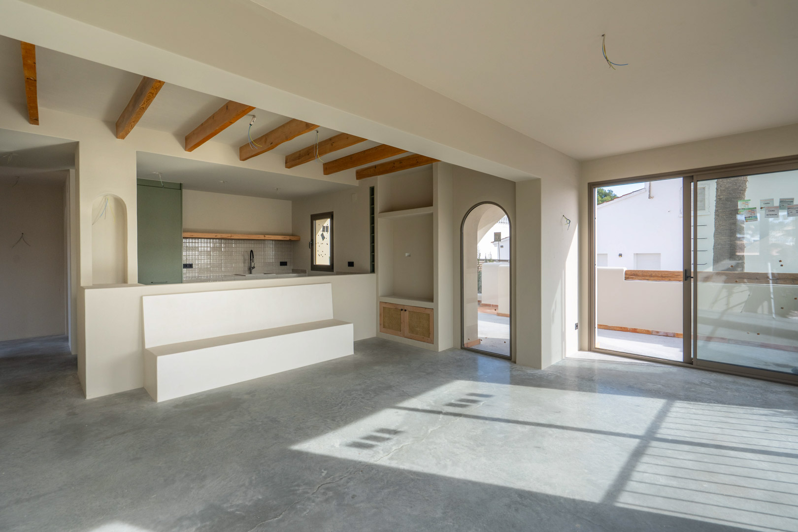 Espace de vie ouvert avec sols en béton poli, poutres en bois apparentes et accès à la terrasse par de larges baies vitrées coulissantes.