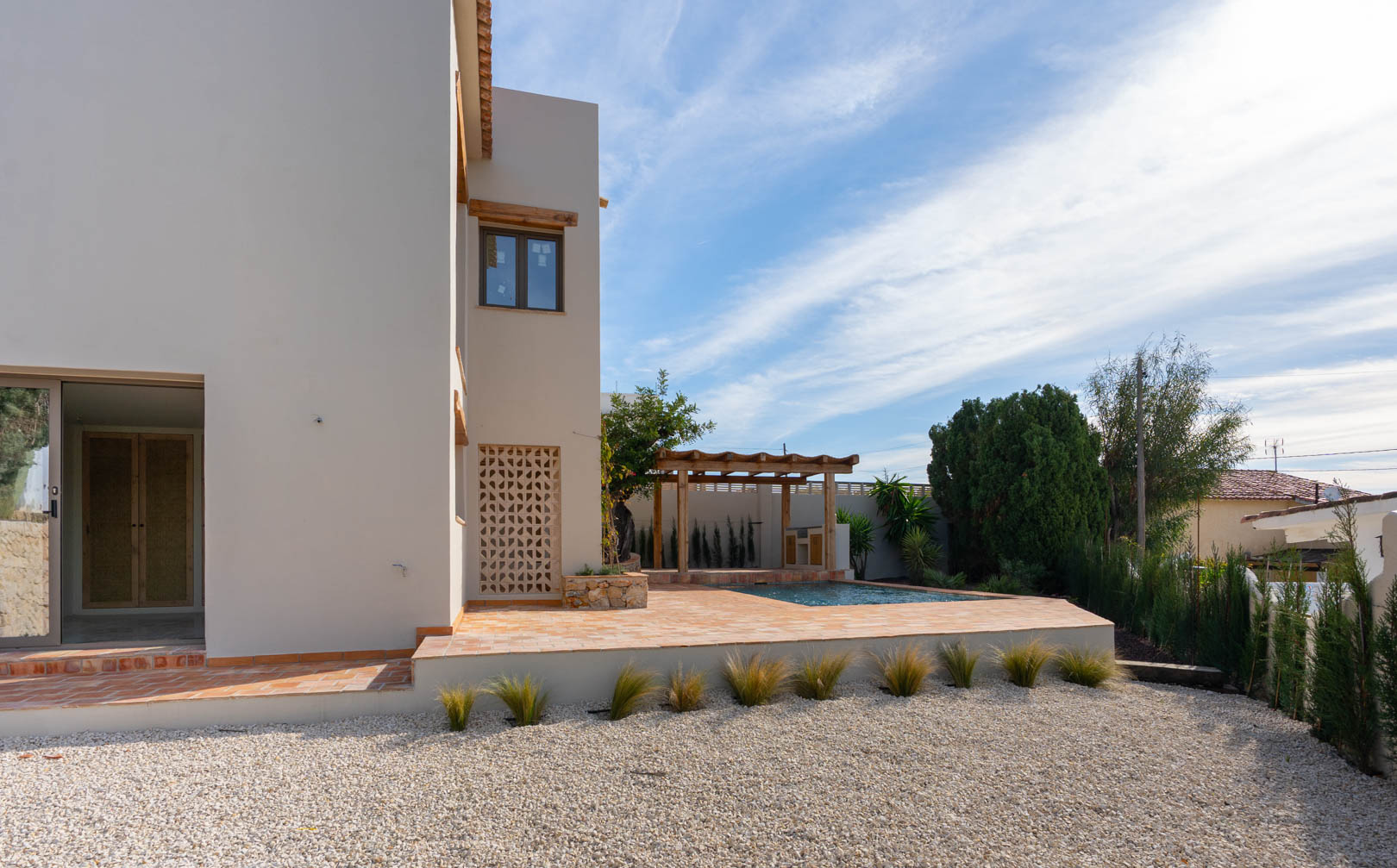Extérieur de la villa avec terrasse en terre cuite, piscine neuve et pergola en bois couvrant l'espace barbecue, le tout bordé d'un jardin paysager en gravier.