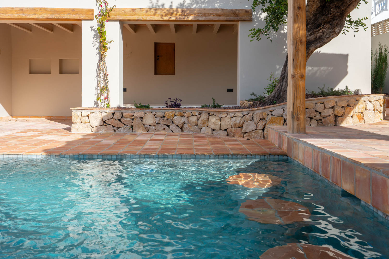 Piscine récemment construite avec assises immergées, entourée de terres cuites, de murets en pierre sèche et de poutres en bois massif en façade.