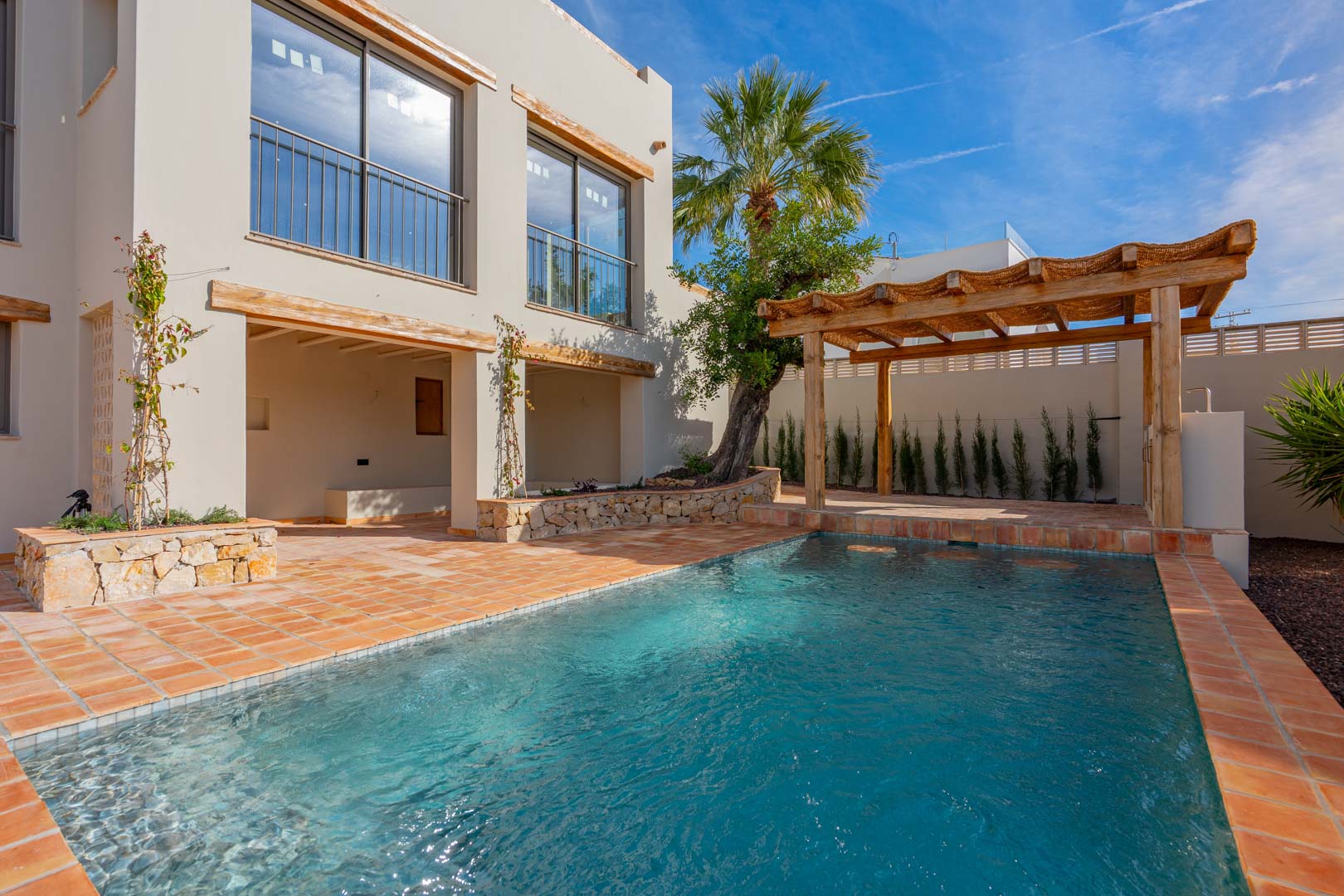 Piscine récemment construite avec terrasse en terre cuite, pergola en bois et murs en pierre naturelle, le tout intégré à l'architecture méditerranéenne.