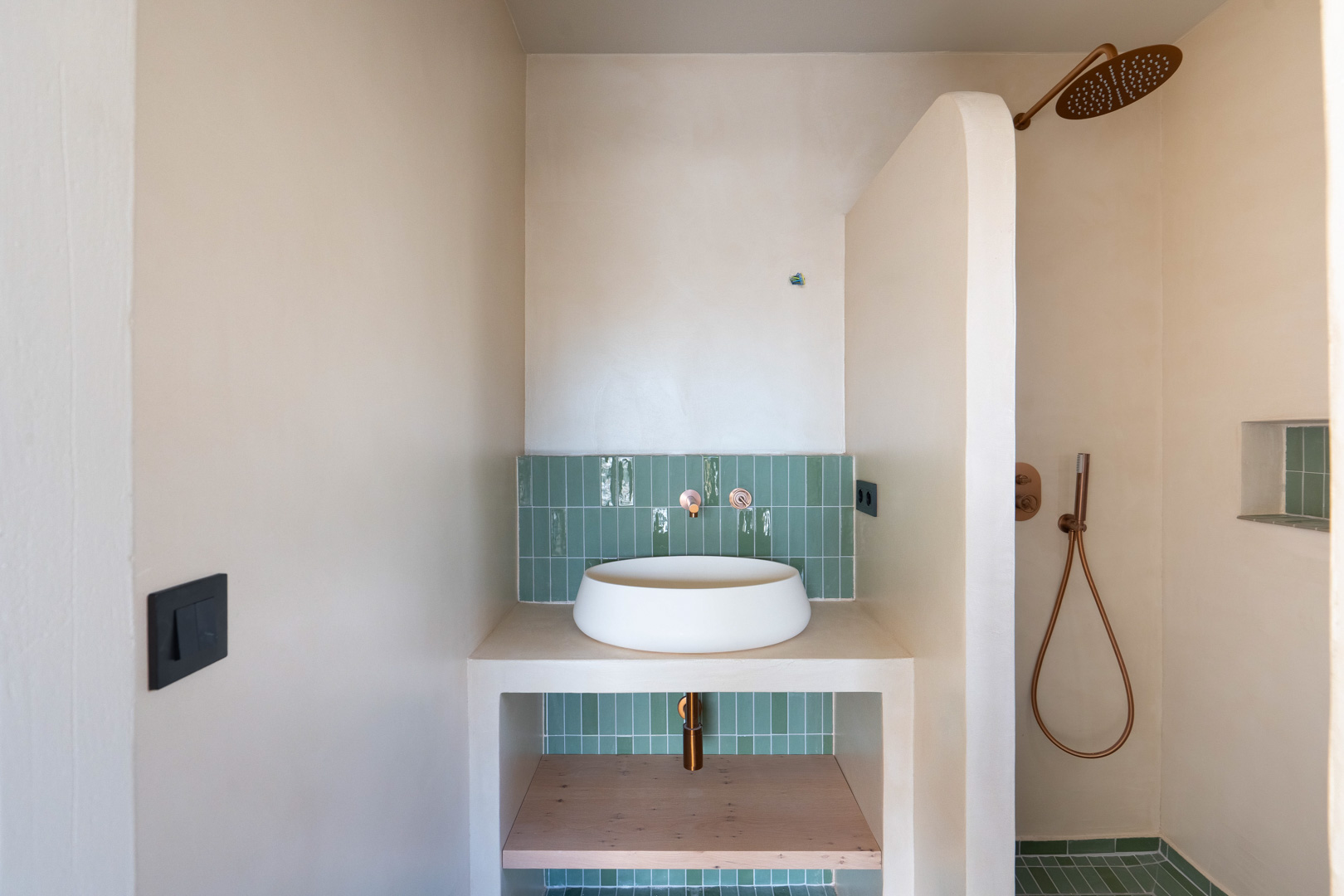 Salle de bain avec vasque à poser, robinetterie en cuivre et faïence verte. Murs en argile et douche à l'italienne avec une paroi maçonnée incurvée.