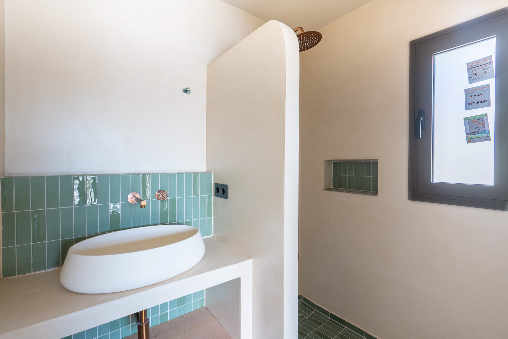 Salle de bain design avec vasque à poser, robinetterie encastrée en cuivre et carrelage vert vertical. Douche à l'italienne avec niche intégrée et finitions en argile matte.