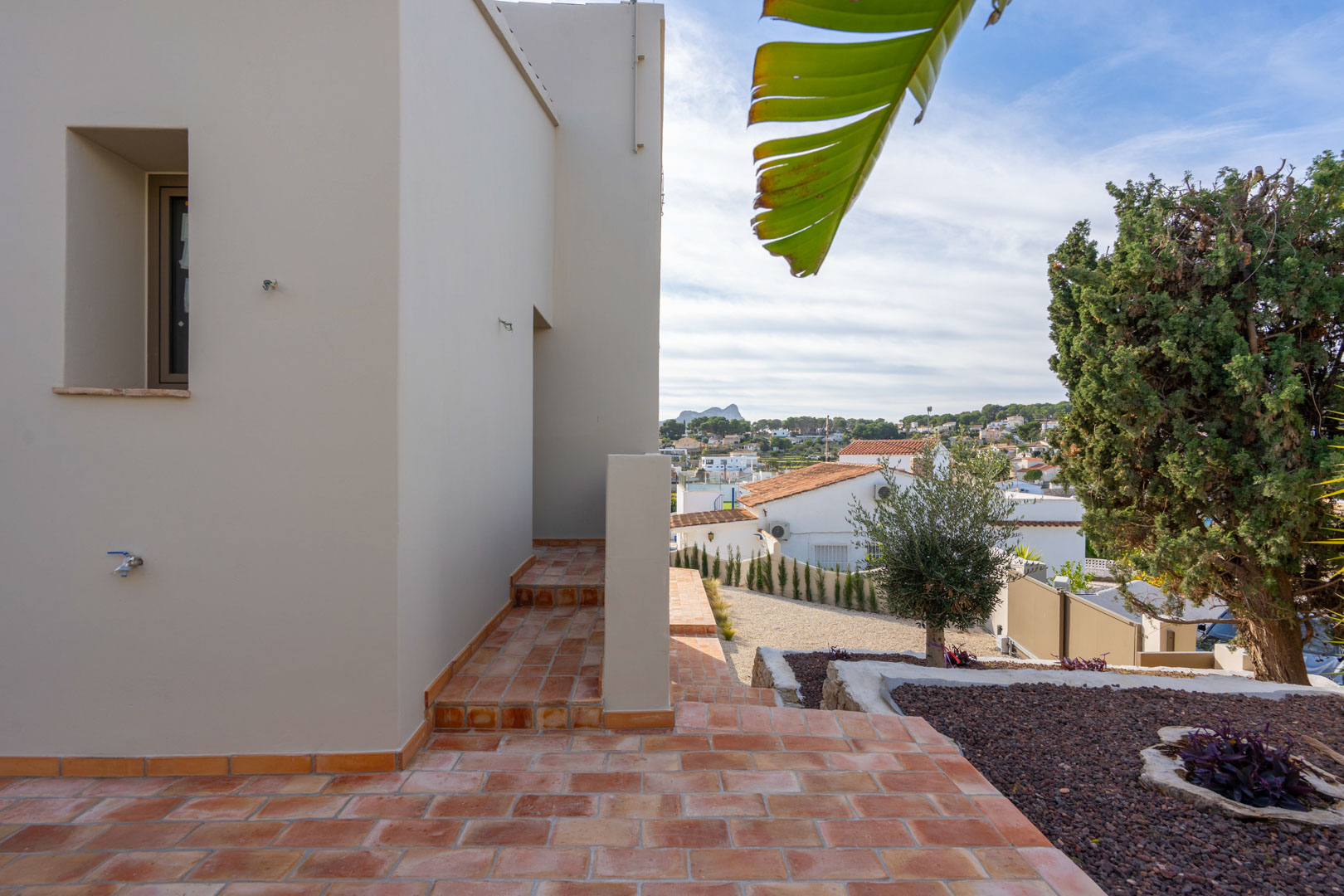 Terrasse extérieure avec carrelage en terre cuite et jardin paysager, offrant une vue dégagée sur le Peñón de Ifach et les environs de Benissa.