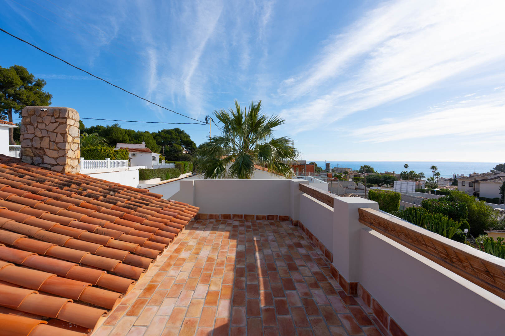 Toit-terrasse avec sol en terre cuite offrant une vue panoramique sur la mer. On y voit une cheminée en pierre naturelle et des tuiles méditerranéennes traditionnelles.