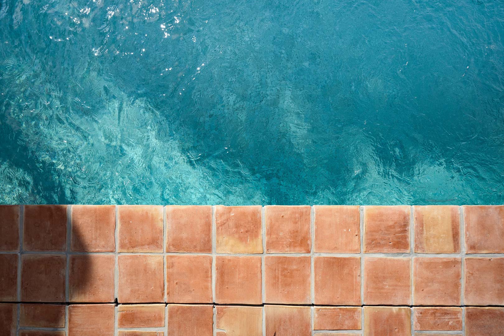 Vue aérienne du bord de la piscine avec des carreaux de terre cuite naturelle et une eau turquoise cristalline, illustrant le style méditerranéen de la villa.