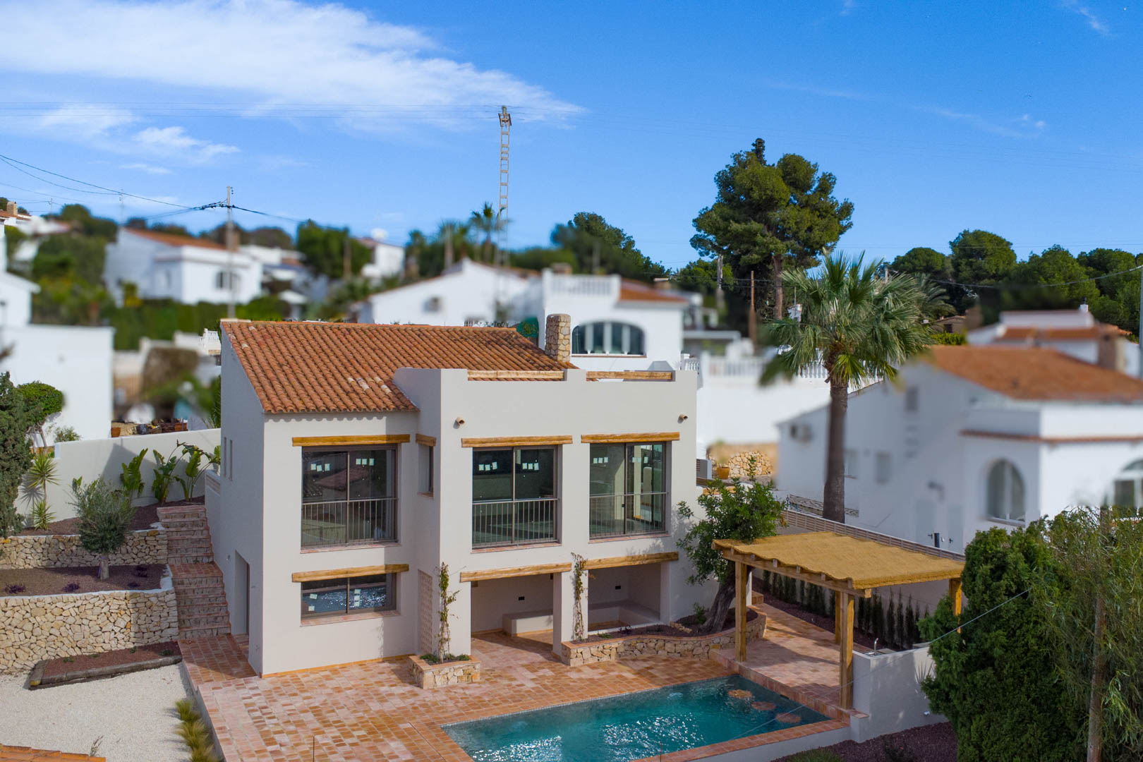 Vue extérieure de la villa méditerranéenne avec ses grandes baies vitrées, son toit en terre cuite, sa piscine et sa pergola en bois sur une terrasse pavée.