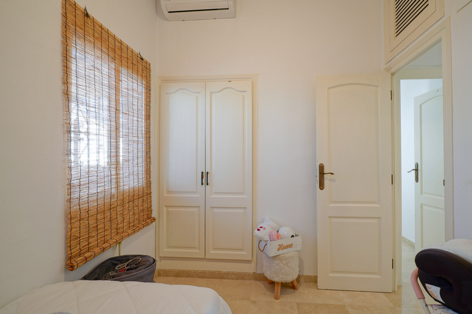 Chambre lumineuse avec armoire encastrée blanche, climatisation individuelle et fenêtre équipée d'un store en bambou naturel.